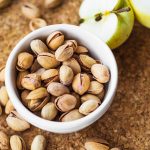 close-up-halved-apple-with-bowl-pistachio-cork-board